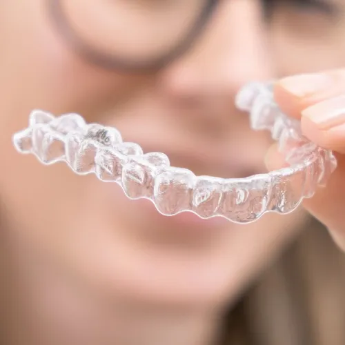 Clear aligner held in front of blurred face in the backrgound.