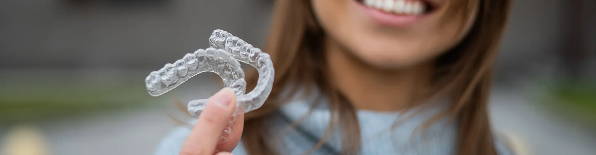 Smiling woman holding clear aligners.