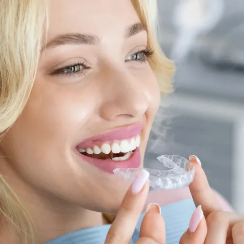 Smiling woman holding a clear Invisalign aligner tray for her orthodontic treatment plan.