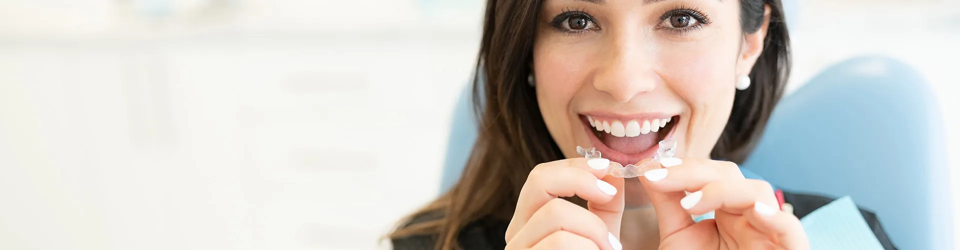 smiling woman placing clear aligner in mouth
