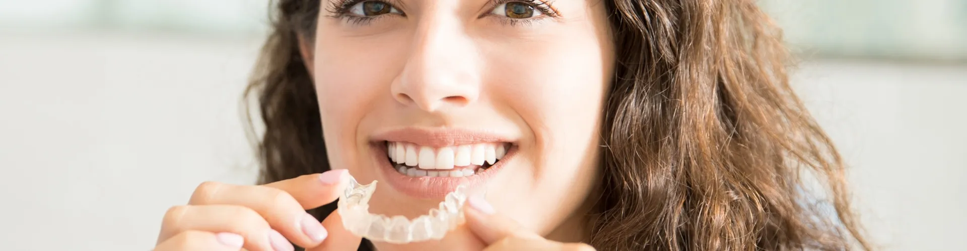 Smiling woman holding clear aligner in front of her mouth.