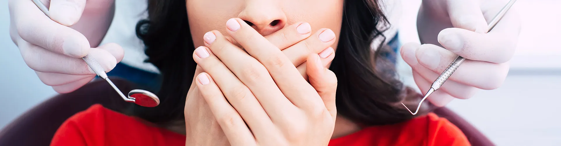 Hands holding dental tools beside woman covering her mouth.