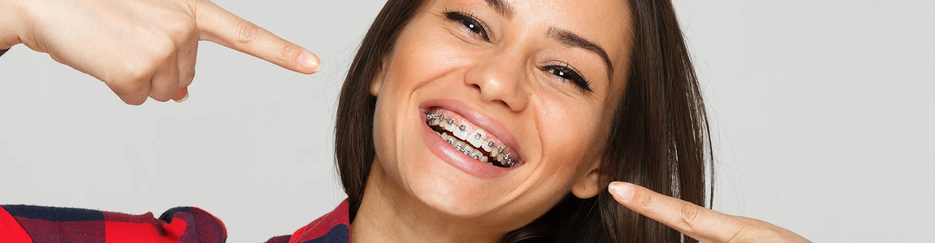 Smiling woman with braces pointing at teeth.