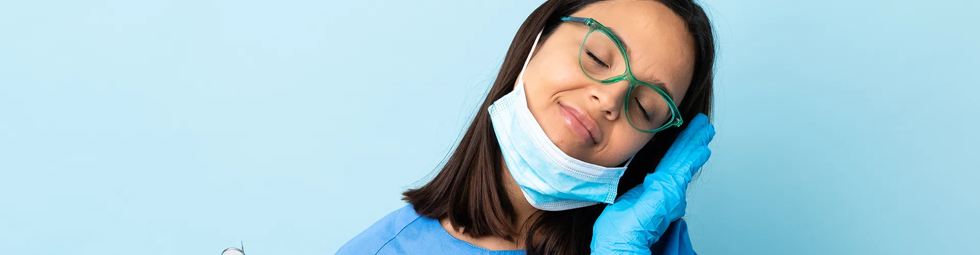 Gloved woman holding dental tools in one hand and resting her head on the palm of the other.