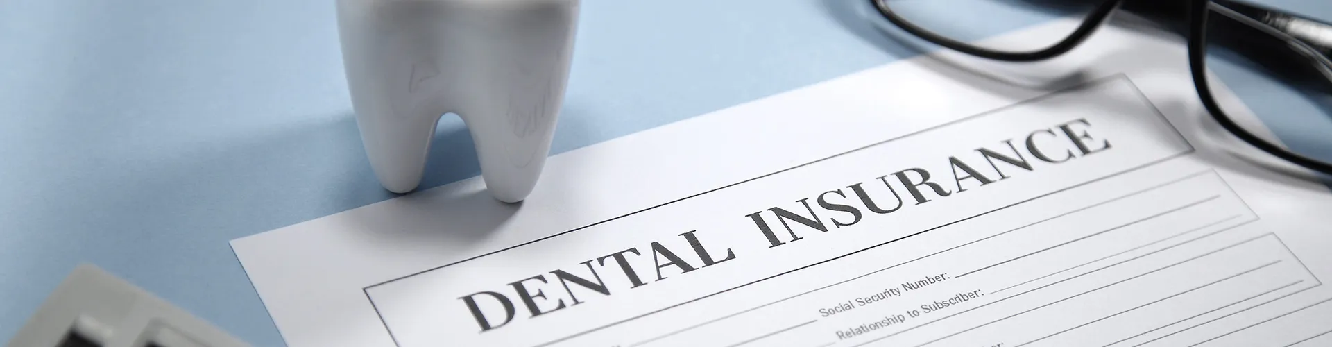 Insurance form and reading glasses next to a tooth model.