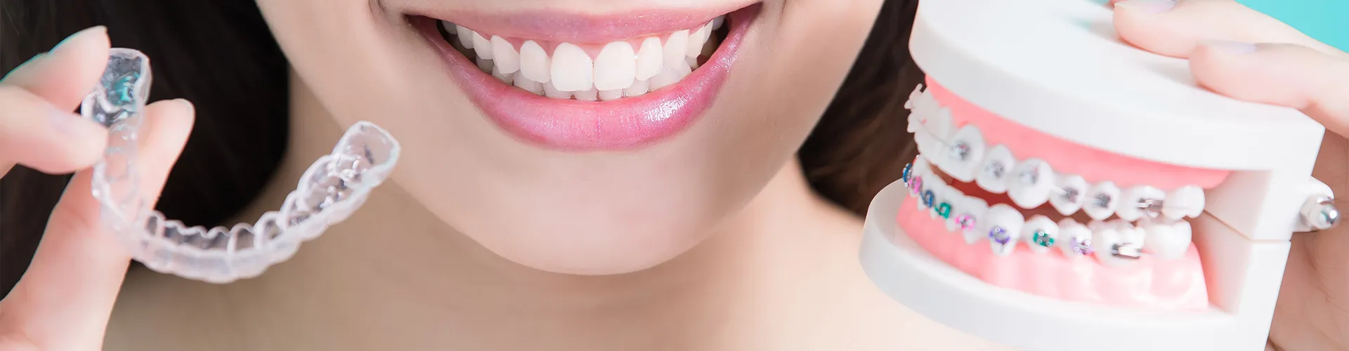 Woman holding braces in one hand and clear aligners in the other.