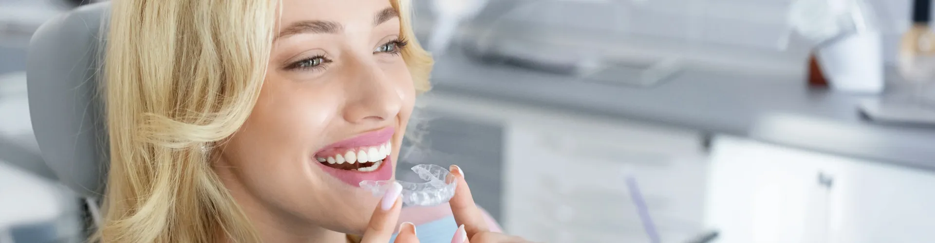 Smiling woman holding a clear Invisalign aligner tray for her orthodontic treatment plan.