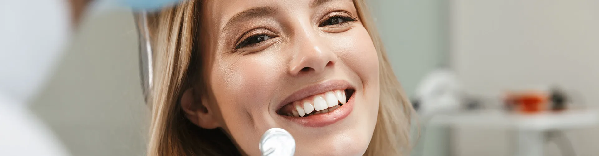 Gloved hands holding dental tools in front of smiling woman.