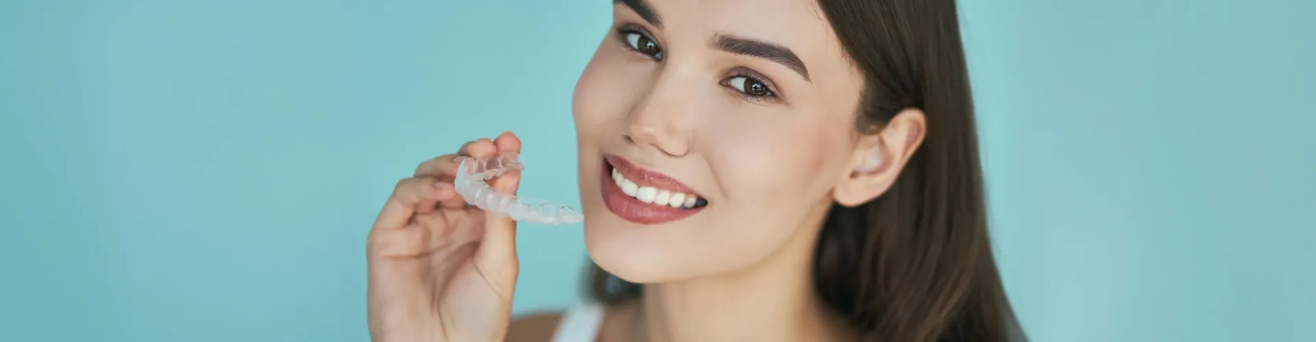 Smiling woman holding a clear Invisalign aligner before starting orthodontic treatment.