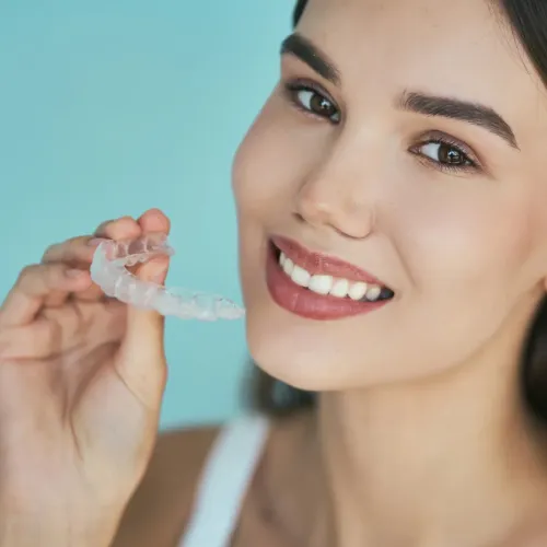 Smiling woman holding a clear Invisalign aligner before starting orthodontic treatment.