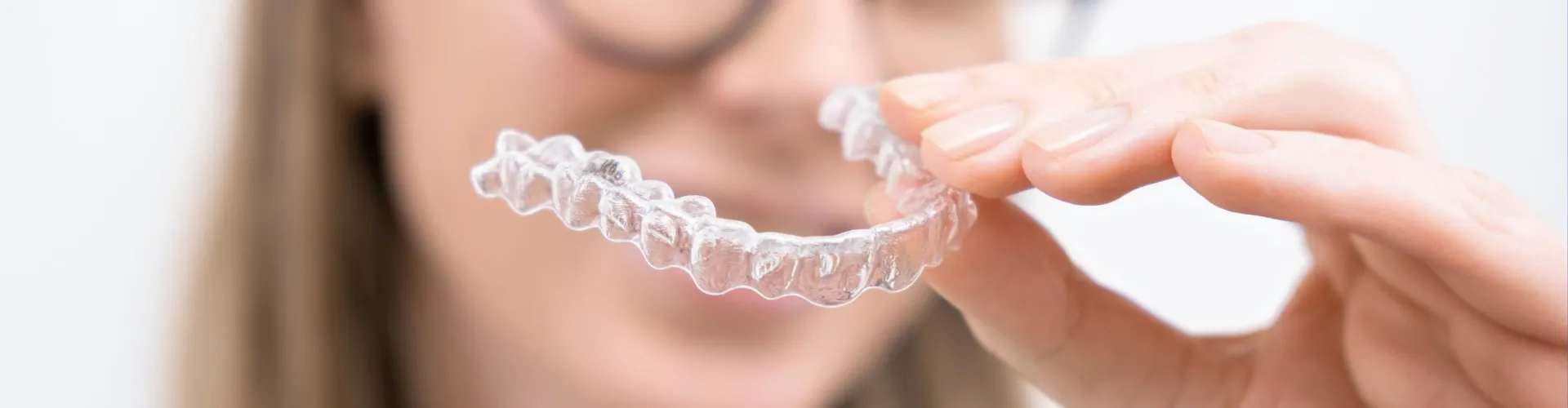 Clear aligner held in front of blurred face in the backrgound.