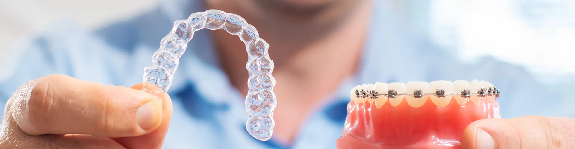 Hands holding clear aligner in one and a model with braces in the other.