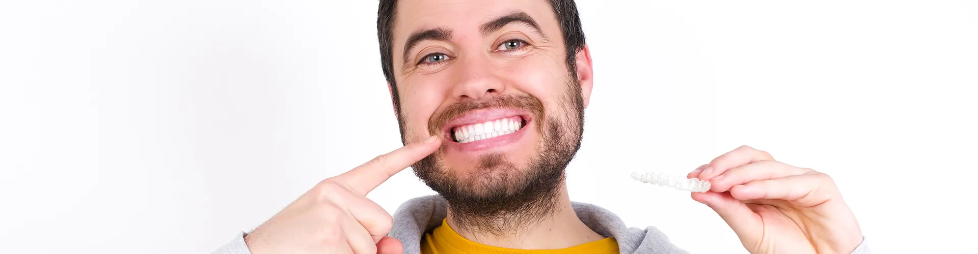 Smiling man pointing at teeth and holding clear aligner.