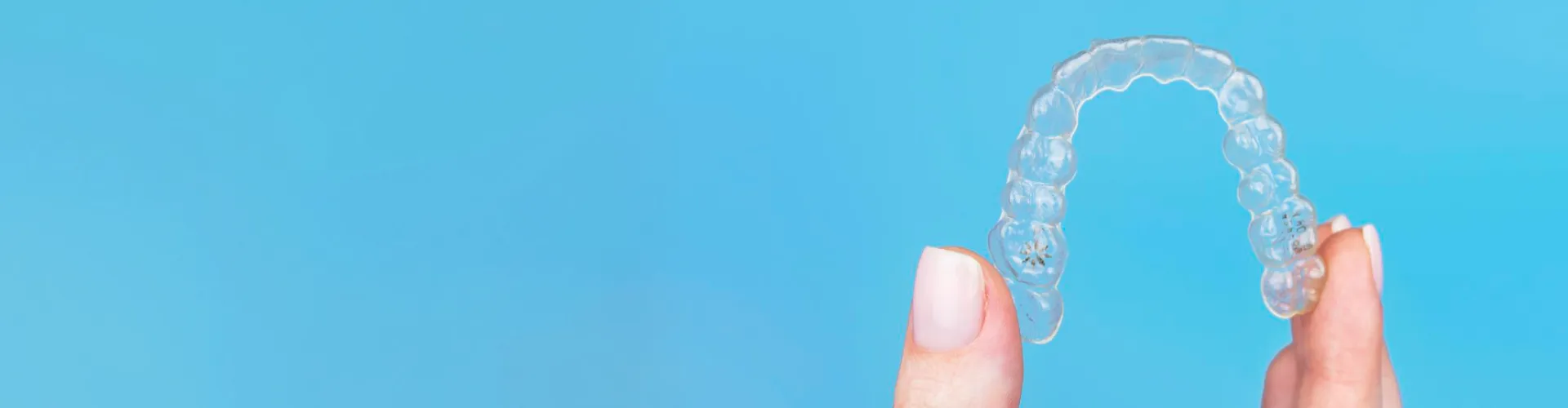 Fingers holding clear aligner.