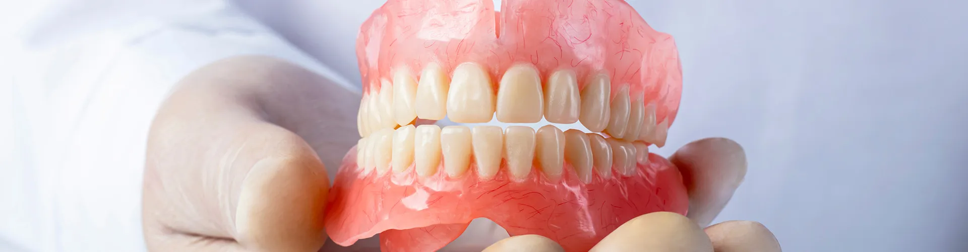 A denture being held by gloved hands.