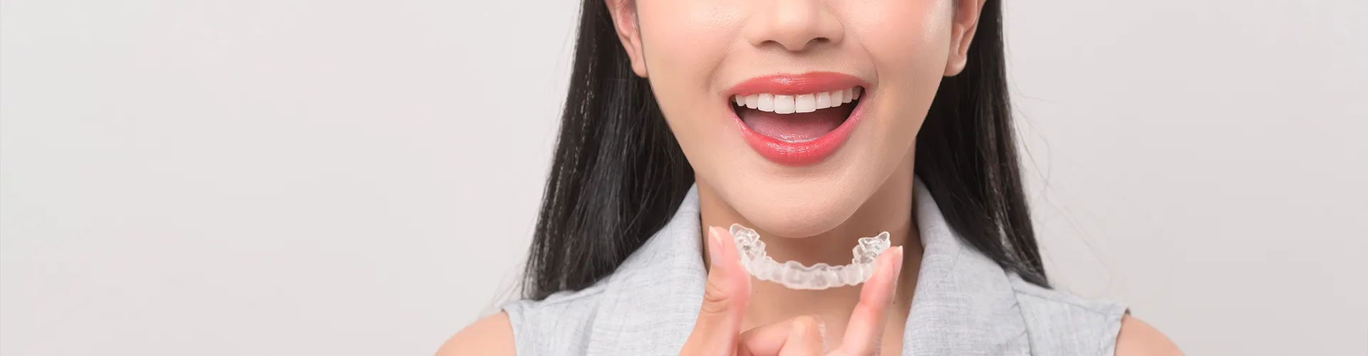 Smiling woman holding clear aligner.