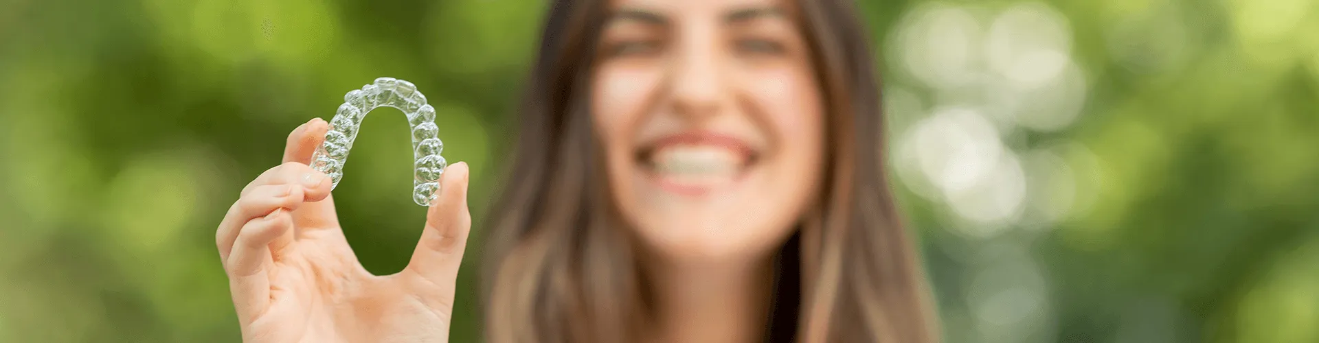 Smiling woman holding clear aligner.