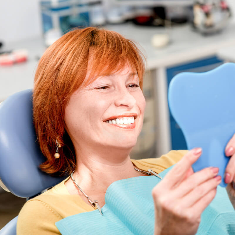 Elderly woman sitting in a dental chair admiring her smile