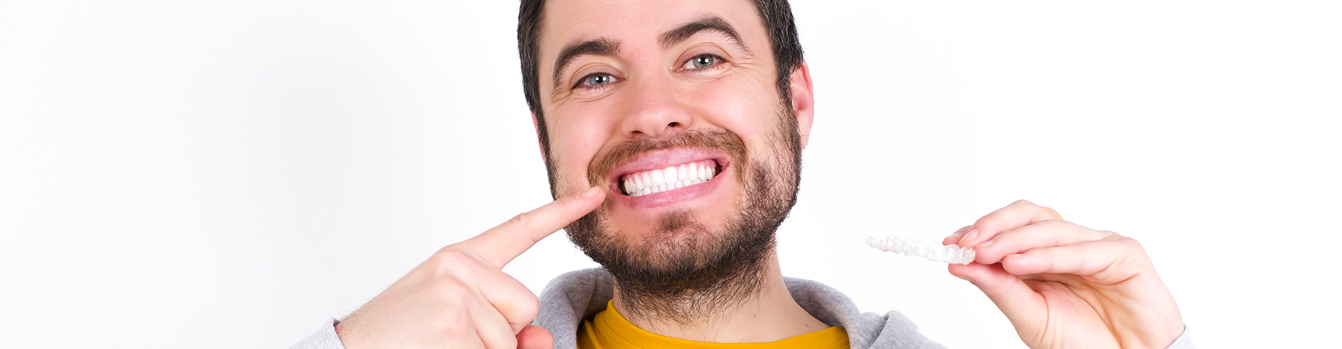 Smiling man pointing at teeth and holding clear aligner.