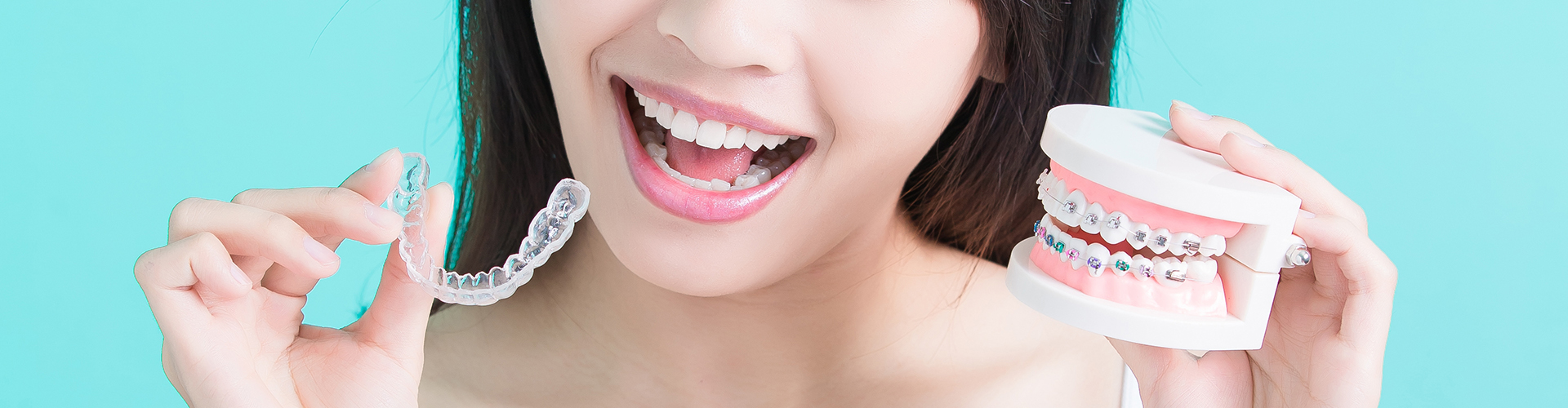 Smiling woman holding clear aligner in one hand and braces model in the other.